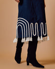 Black skirt with white decorative patterns and tassels worn by a person on a beige background