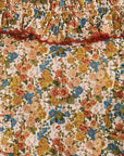 A close-up of a floral fabric with a smocked elastic waistband and ruffled trim. The pattern features a dense mix of yellow, orange, blue, and pink flowers with green leaves on a cream background.