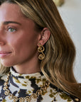 A close-up lifestyle shot of a woman wearing a matching gold spiral drop necklace and matching spiral drop earrings, paired with a high-neck tie-dye top.
