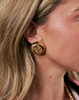 A close-up of a woman's ear wearing a chunky, polished gold rose-shaped stud earring.
