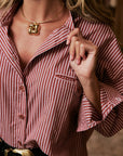 A close-up lifestyle shot of a woman wearing a red and white vertically striped button-down shirt, a gold chain necklace with a gold initial 'M' pendant, and a black belt with a gold buckle.
