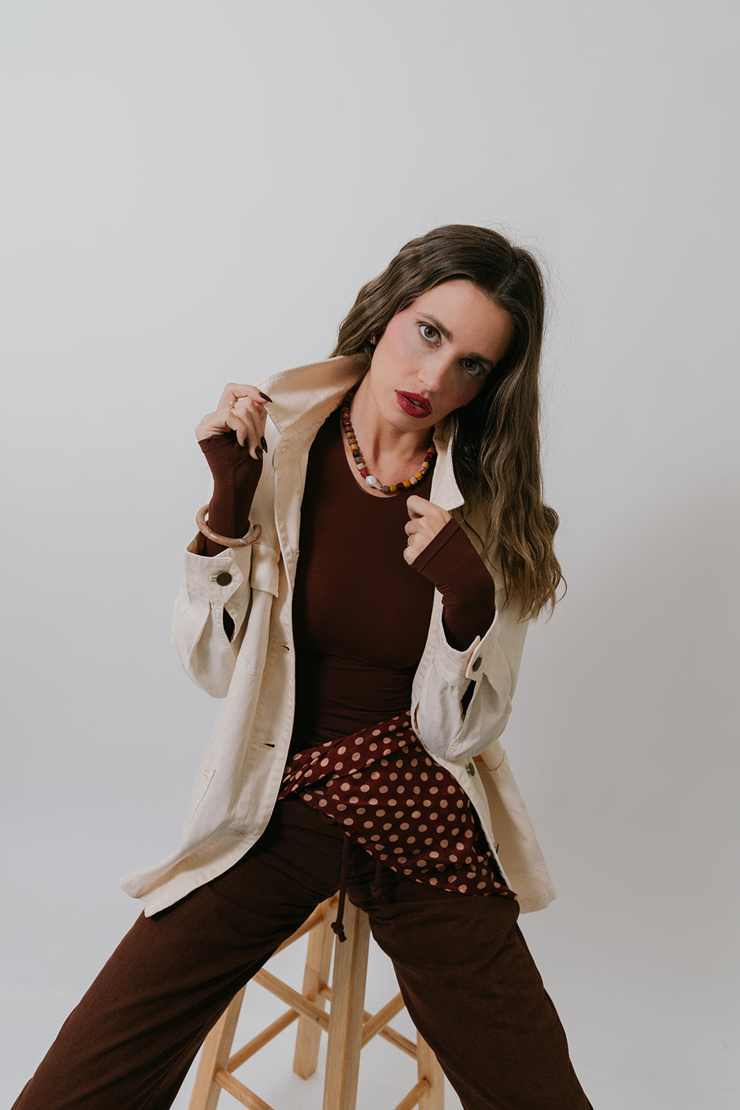 Woman posing in a stylish outfit with a beige jacket and brown pants against a plain background