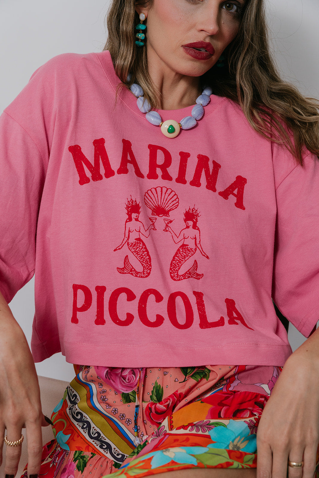 Person wearing a pink sweatshirt with 'MARINA PICCOLA' text and mermaid graphics. close up