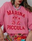 Person wearing a pink sweatshirt with 'MARINA PICCOLA' text and mermaid graphics. close up