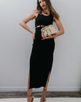 Woman in a black dress holding a gold clutch against a white wall