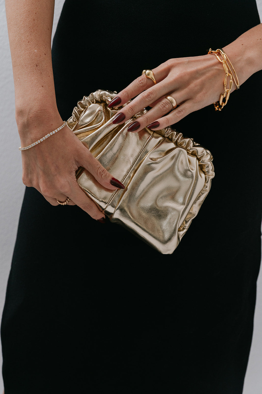 Gold clutch held by a hand with red nail polish against a black background