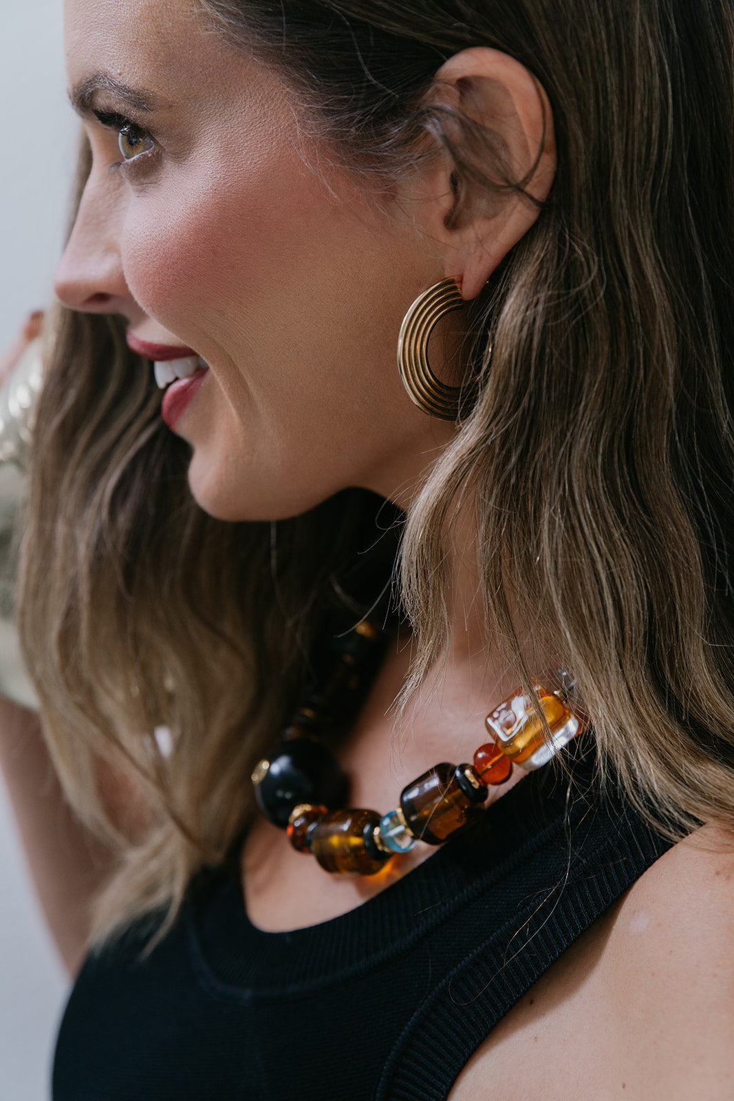 Woman wearing gold hoop earrings and a colorful beaded necklace.