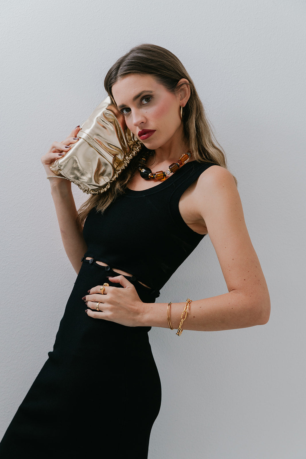 Woman in a black dress and Desert Mirage Collar Necklace holding a gold clutch against a plain background