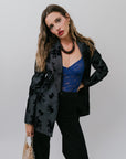 Woman wearing a black floral blazer over a blue top with a plain background