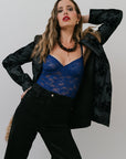 Woman wearing a black jacket and blue top against a plain background