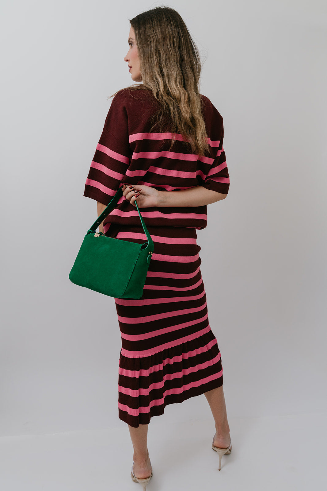 Woman wearing a striped set holding a green bag against a white background, back