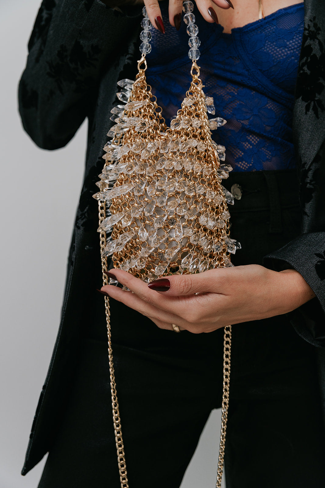 Person holding a sparkling handbag with a gold chain strap against a neutral background