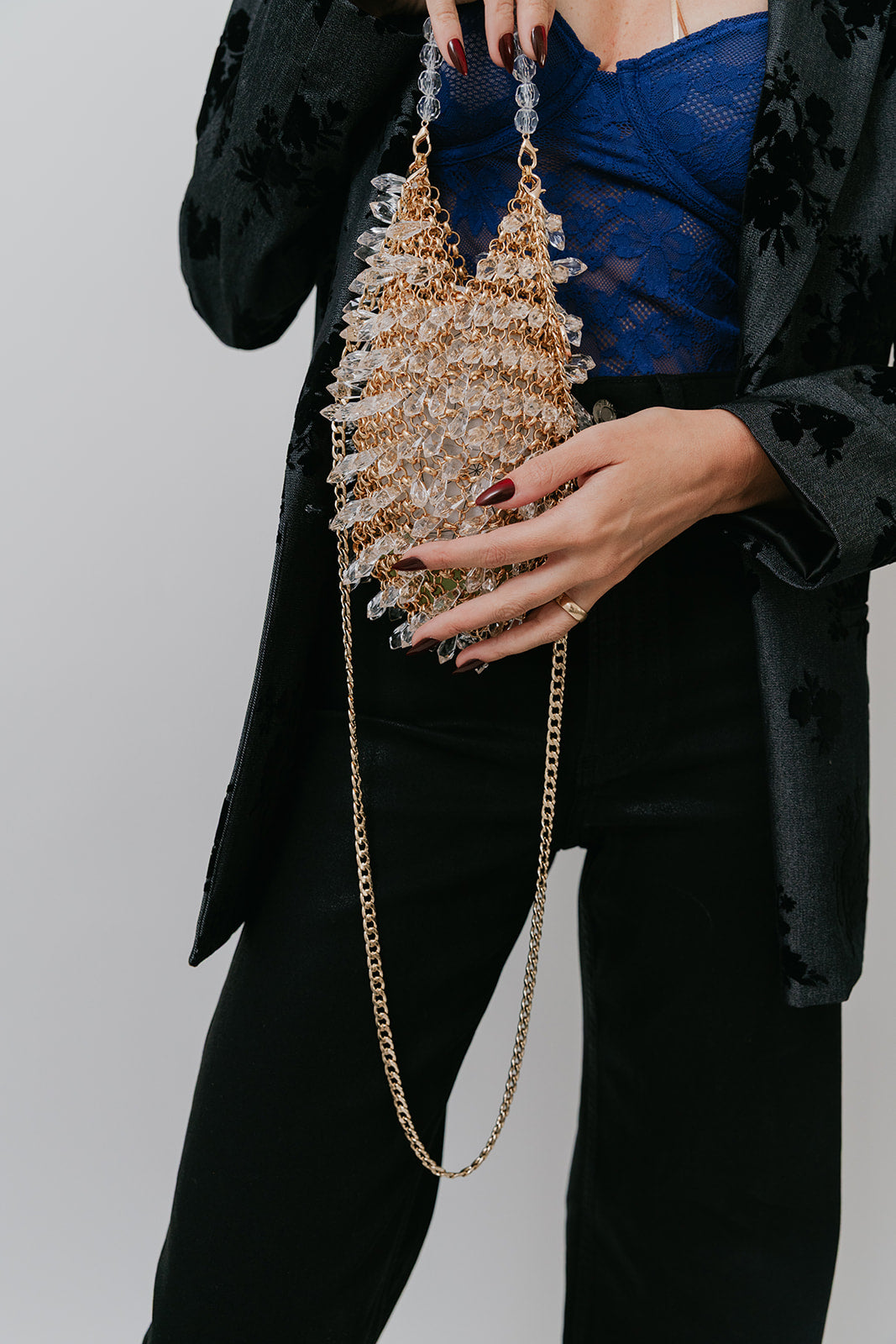 Person holding a decorative handbag with a gold chain against a neutral background