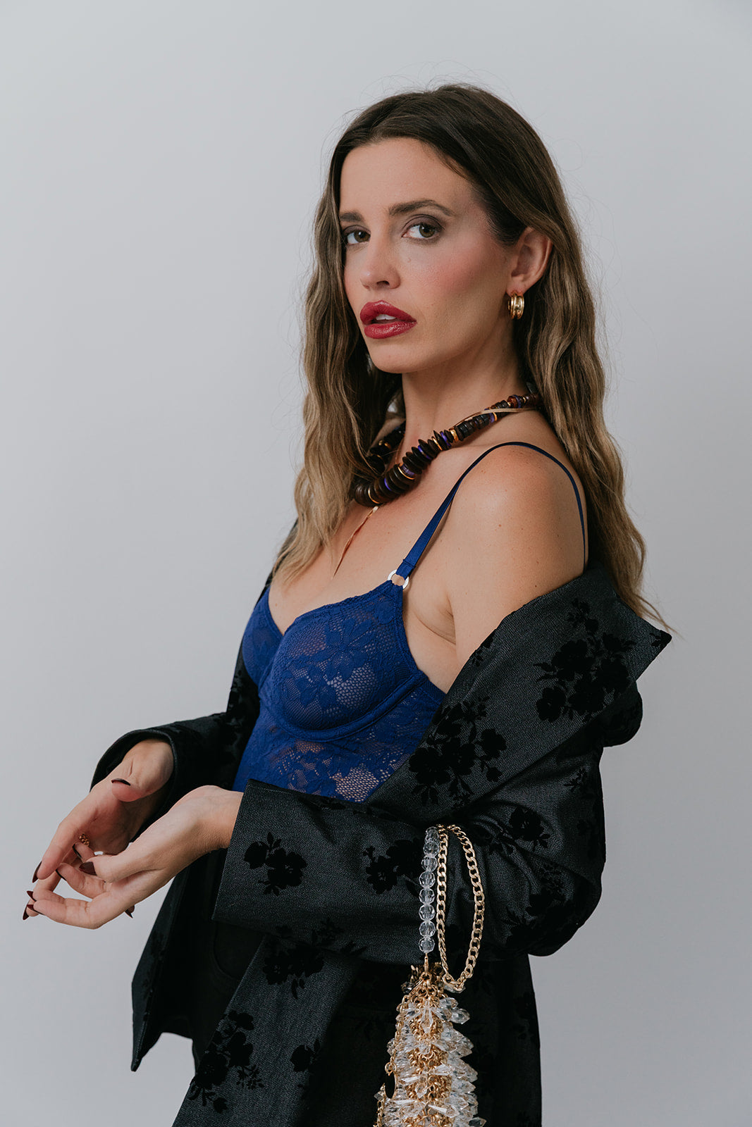 Woman wearing a blue lace top and black floral blazer against a plain background, side view