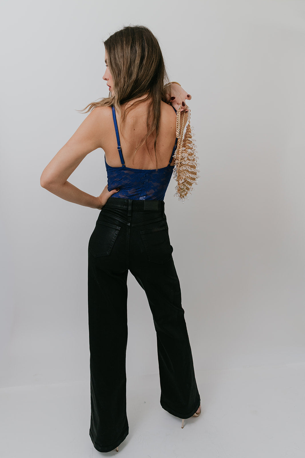 Woman wearing a blue top and black flared pants against a white background, back view