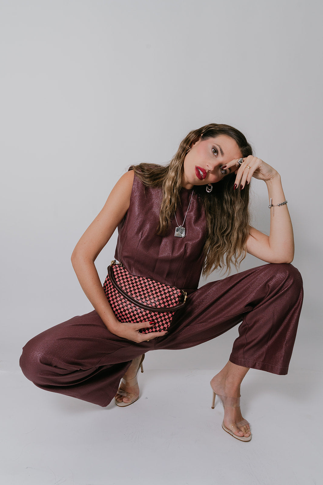 Woman in a maroon outfit with a checkered handbag posing against a plain background
