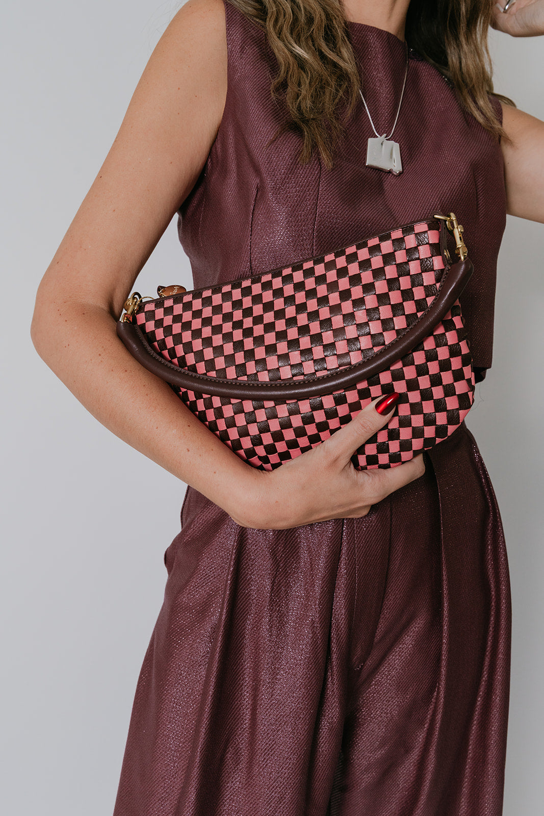 Person holding a pink and raisin checkered bag against a plain background