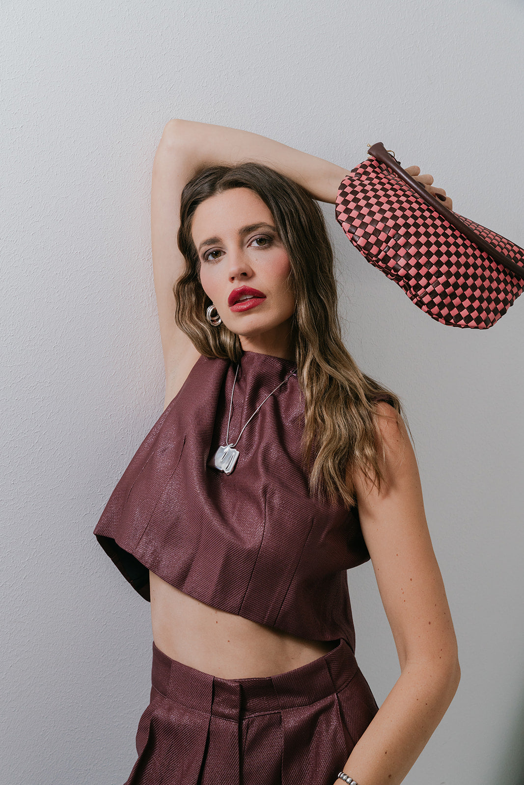 Woman in a maroon outfit holding a patterned bag against a plain background