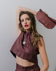 Woman in a maroon outfit holding a patterned bag against a plain background
