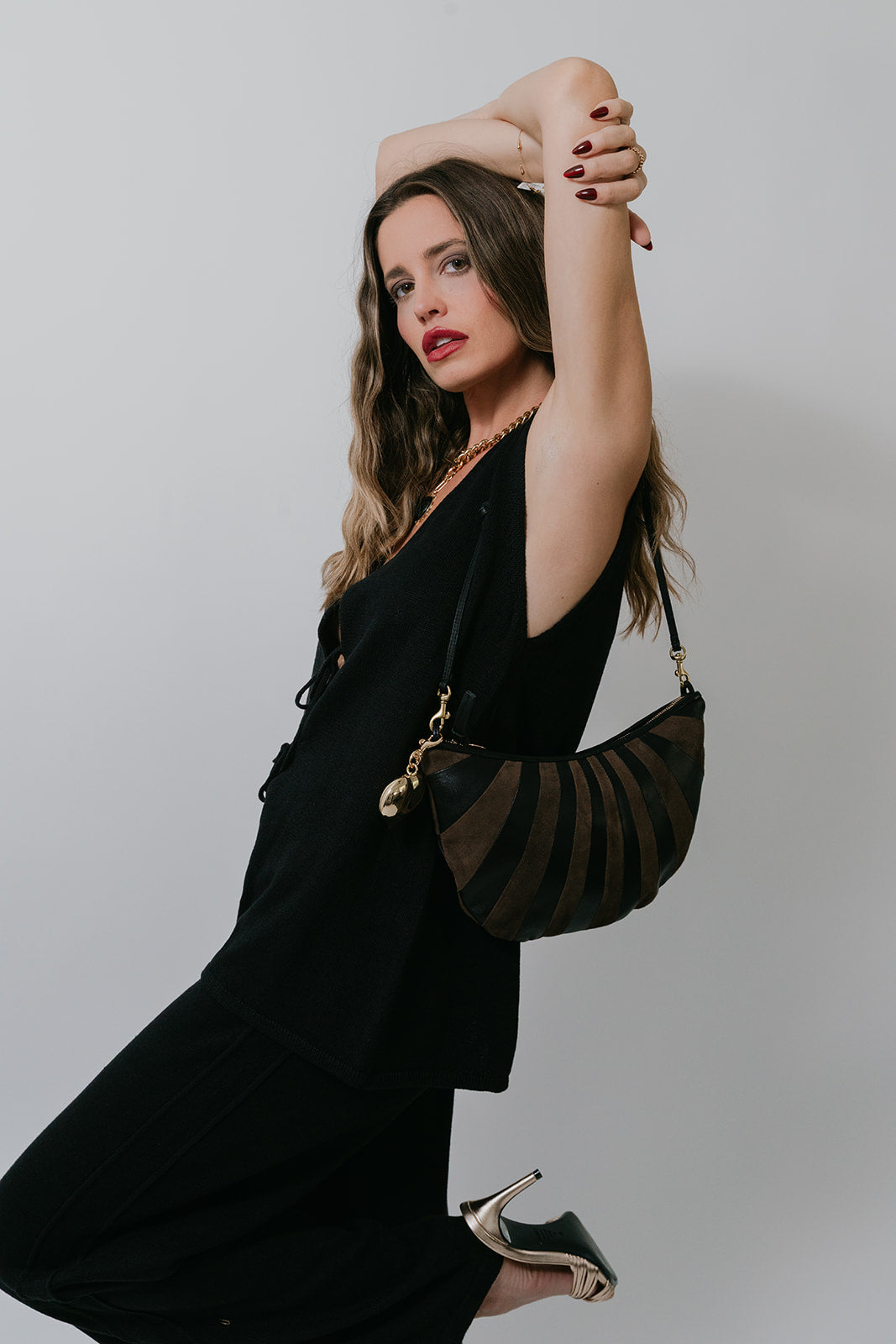 Woman in a black set holding a black and brown handbag against a plain background, side view
