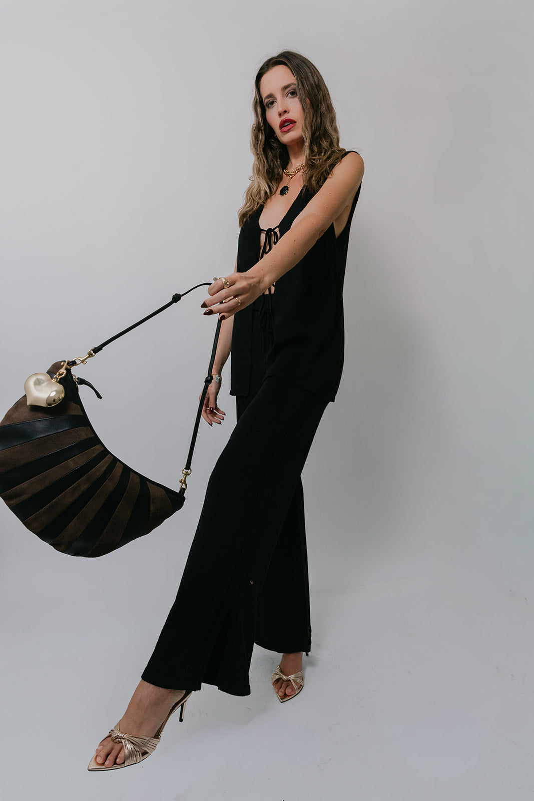 Woman in a Poppy Pant and tank holding a black handbag against a plain background