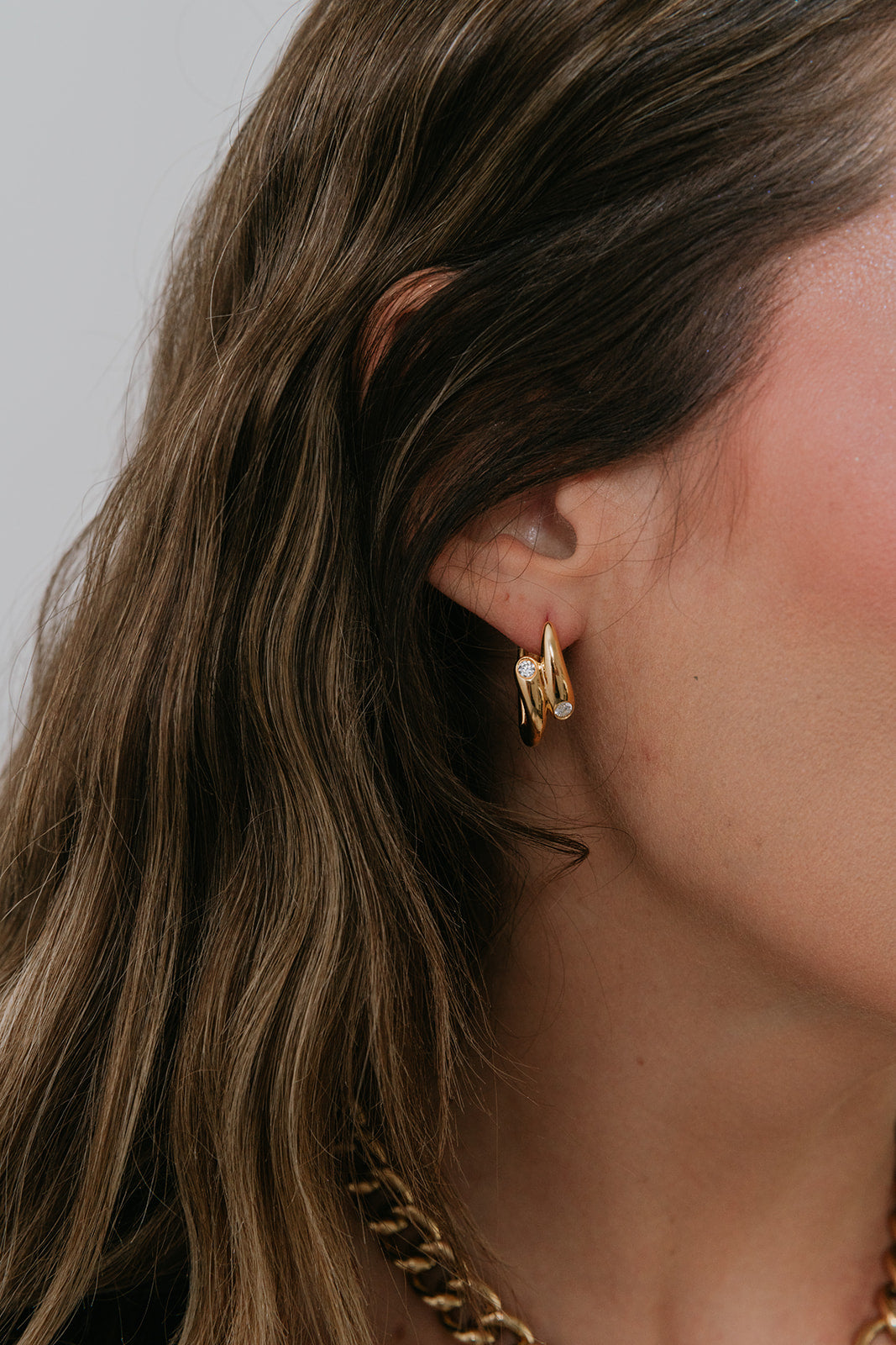 Close-up of a person wearing gold hoop earrings with a neutral background