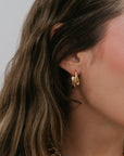 Close-up of a person wearing gold hoop earrings with a neutral background