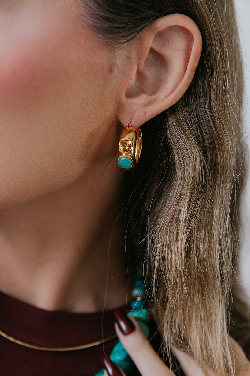 Close-up of a person wearing gold hoop earrings with turquoise stones.