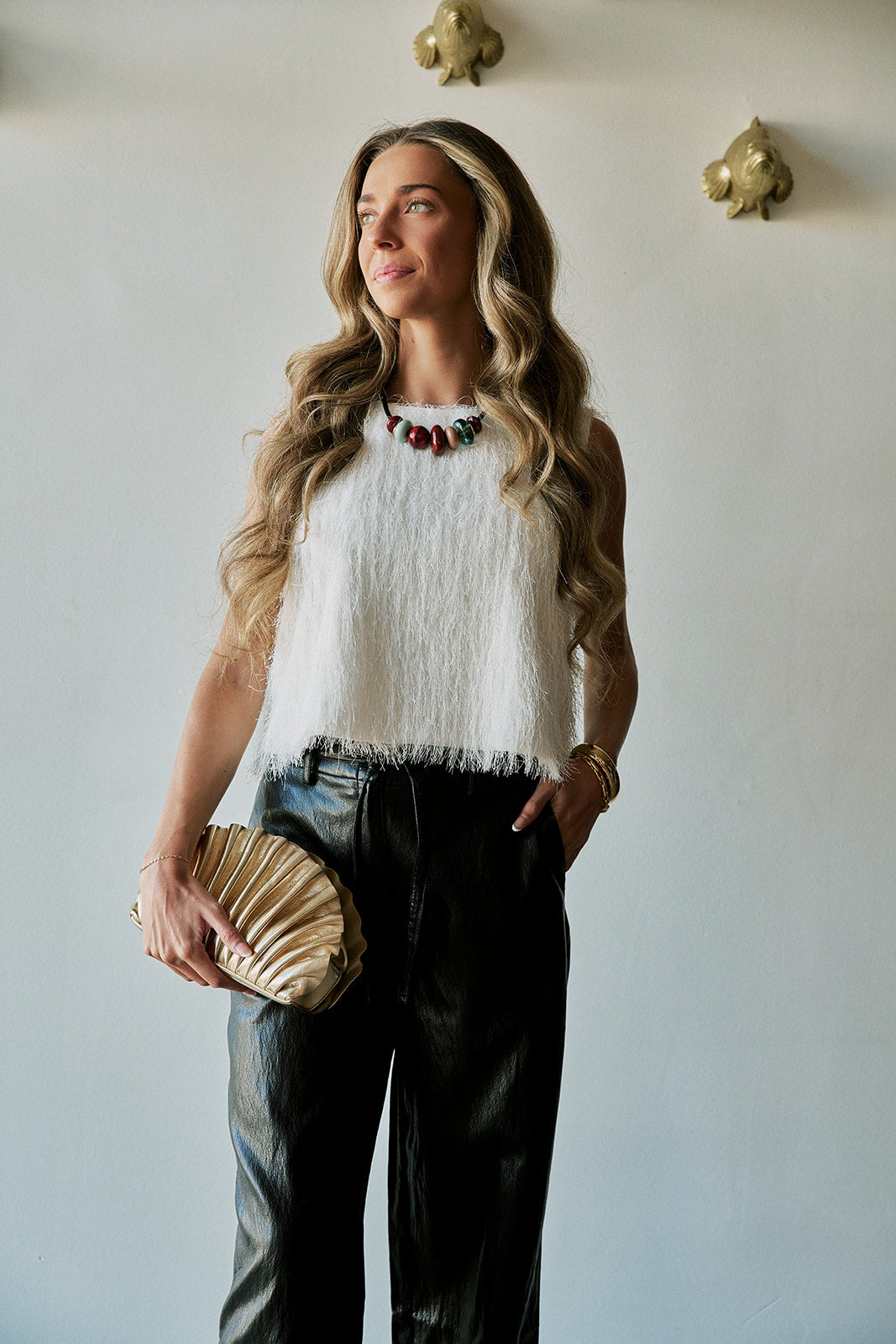 model wearing a statement necklace with a white tassel top and black bottoms holding a gold clutch