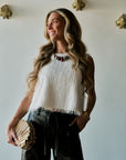 model wearing a statement necklace with a white tassel top and black bottoms holding a gold clutch
