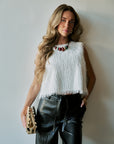 model wearing a statement necklace with a white tassel top and black bottoms holding a gold clutch