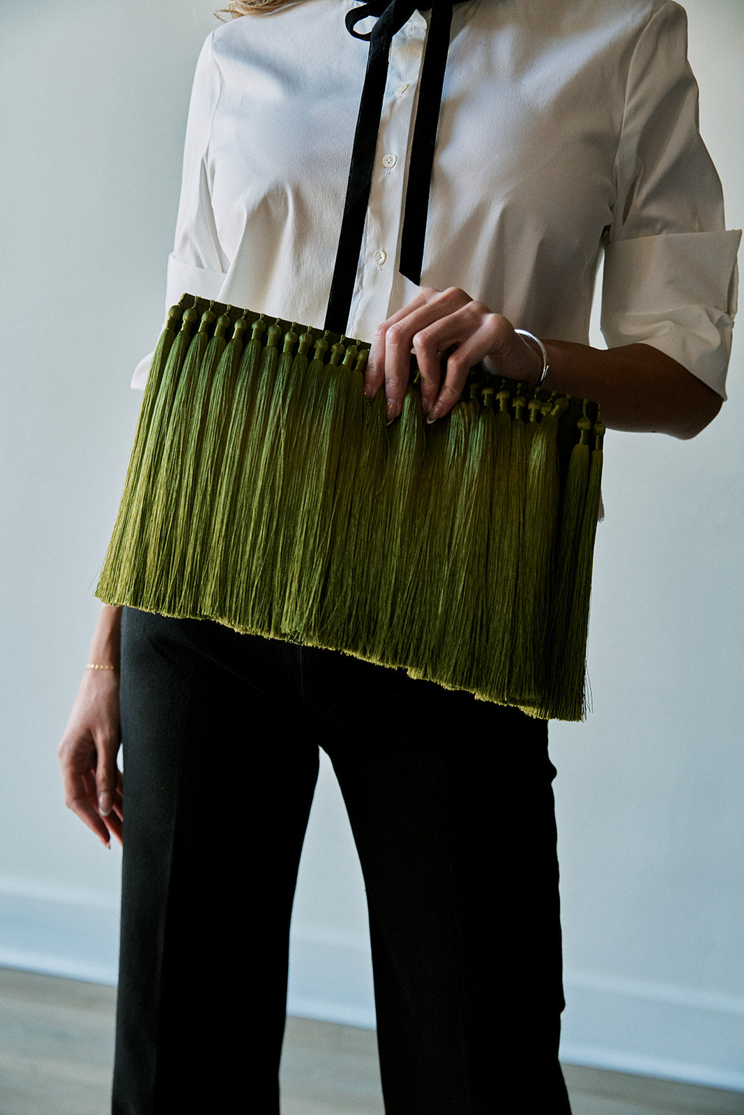 model holding an oversized green tassel clutch while wearing a black and white top with black bottoms 