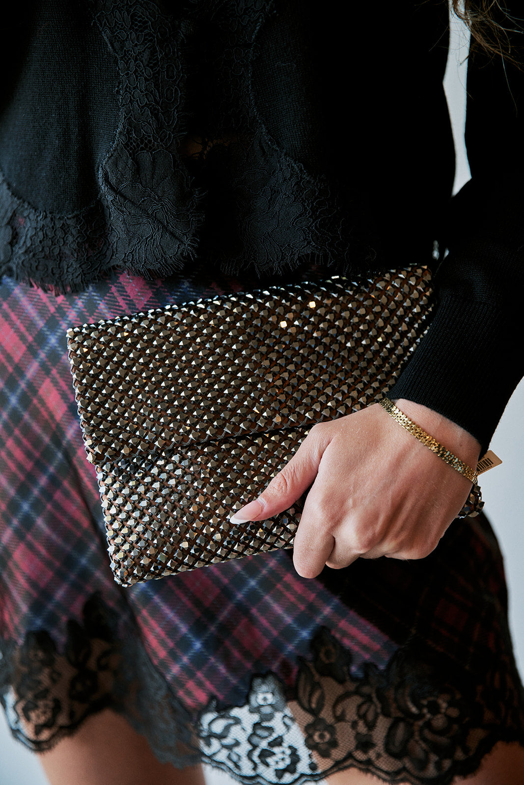 model holding a sequin clutch while wearing a plaid lace trim skirt and black sweater 