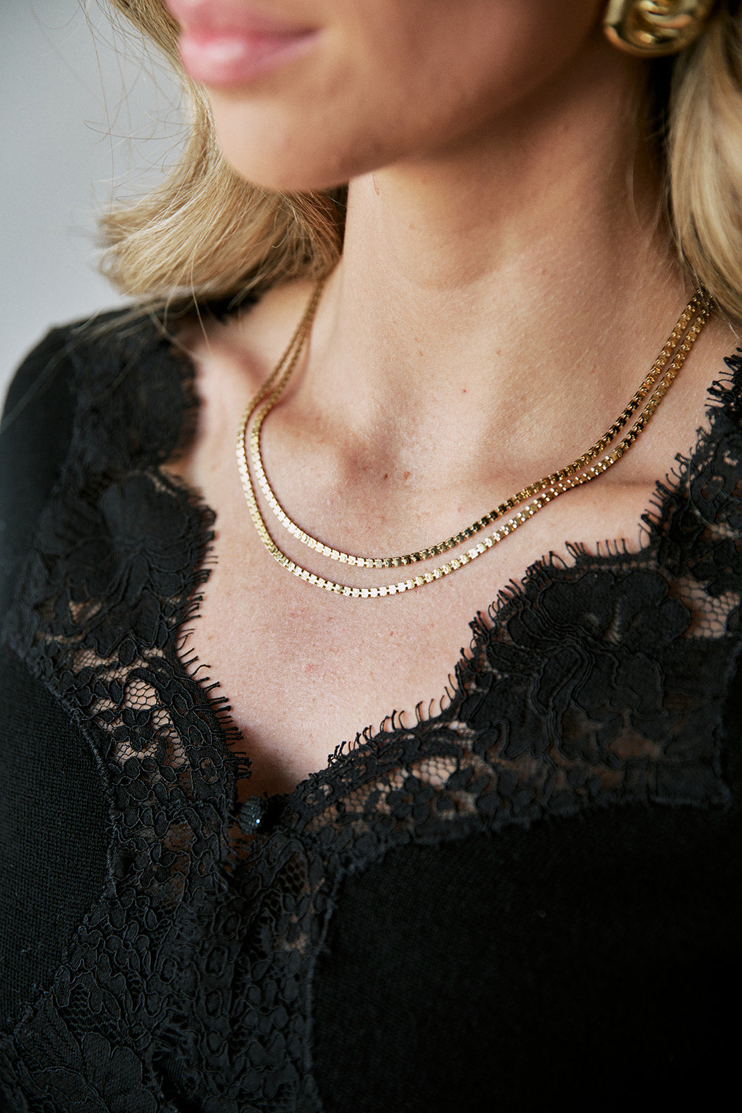 Close-up of a woman wearing a delicate double layer gold necklaces layered over a black lace top.