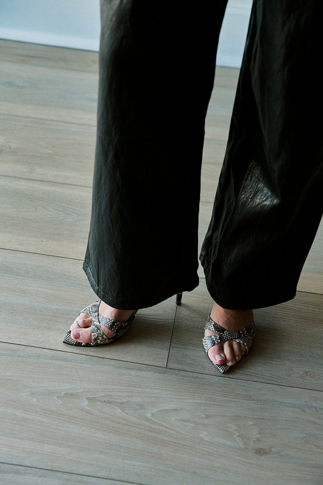 model wearing snake heels with black pants on light colored floor