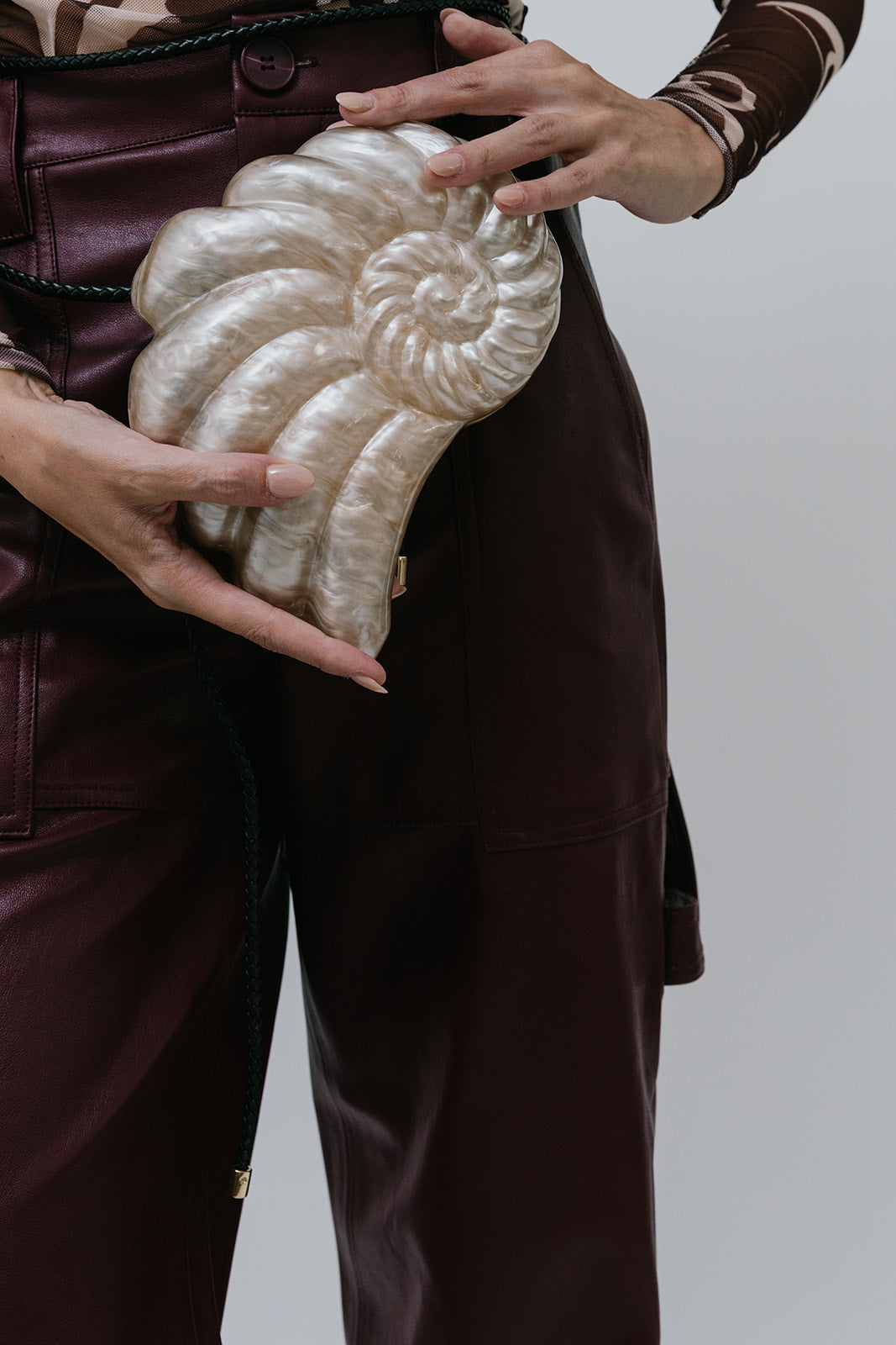 Person holding a decorative white shell-shaped clutch against a plain background