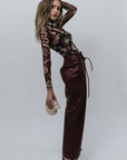 Woman wearing a patterned top and high-waisted pants against a white background