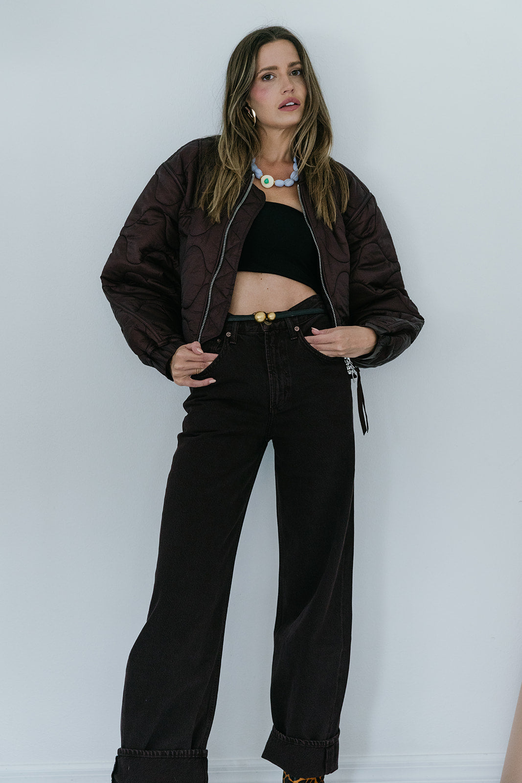 Woman wearing a brown jacket and dark brown pants against a white background
