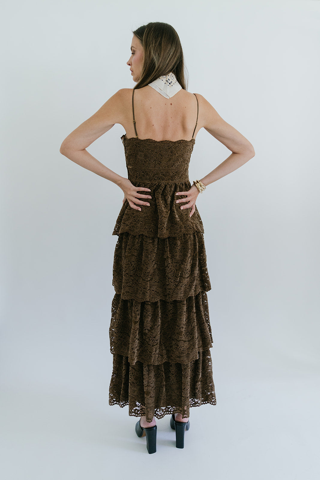 Woman wearing a brown tiered dress against a white background, back view