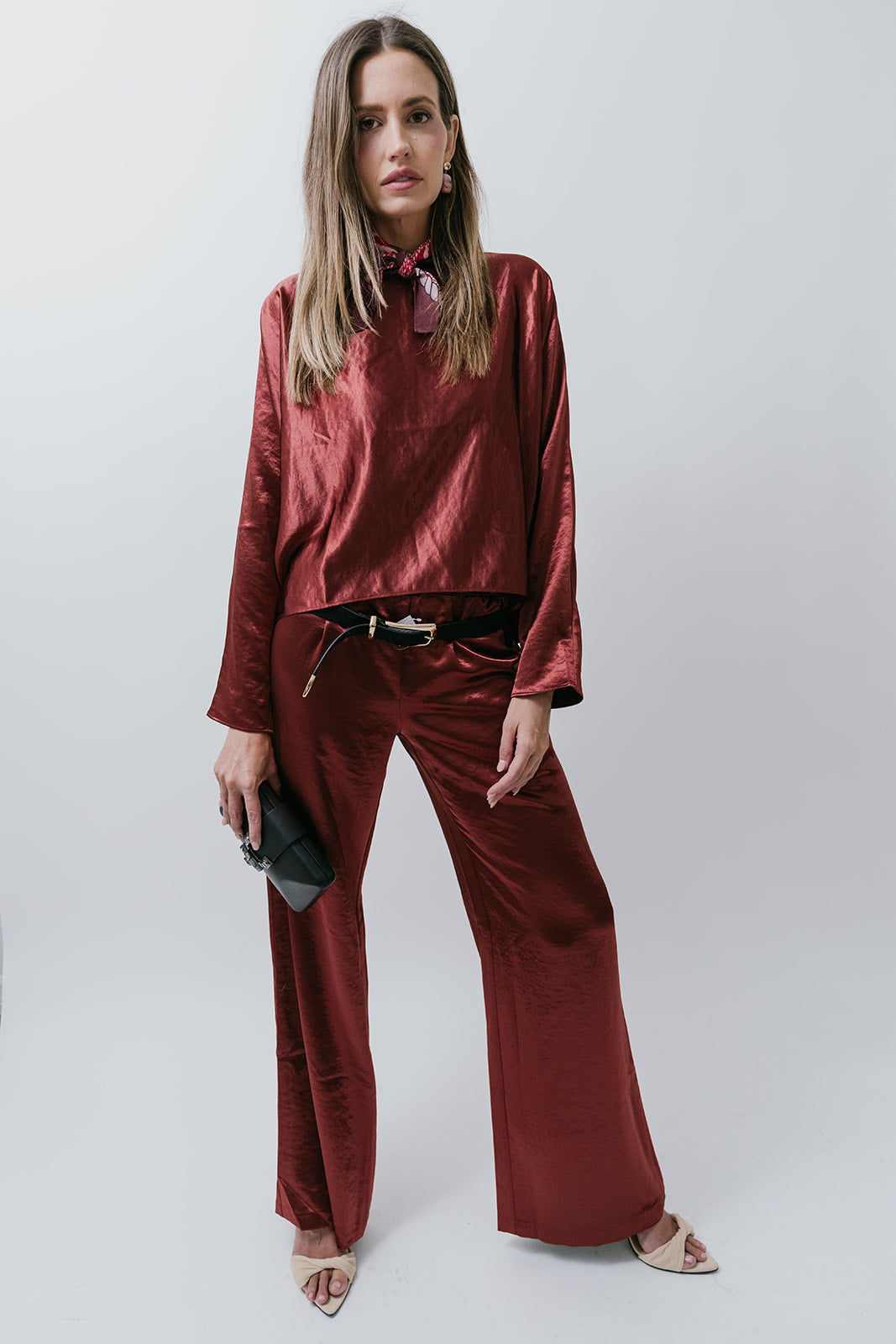 Woman wearing a burgundy satin blouse and pants against a white background