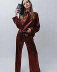 Woman in a burgundy satin outfit and black clutch posing against a white background