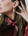 Close-up of a woman wearing pink earrings with a red scarf around her neck.