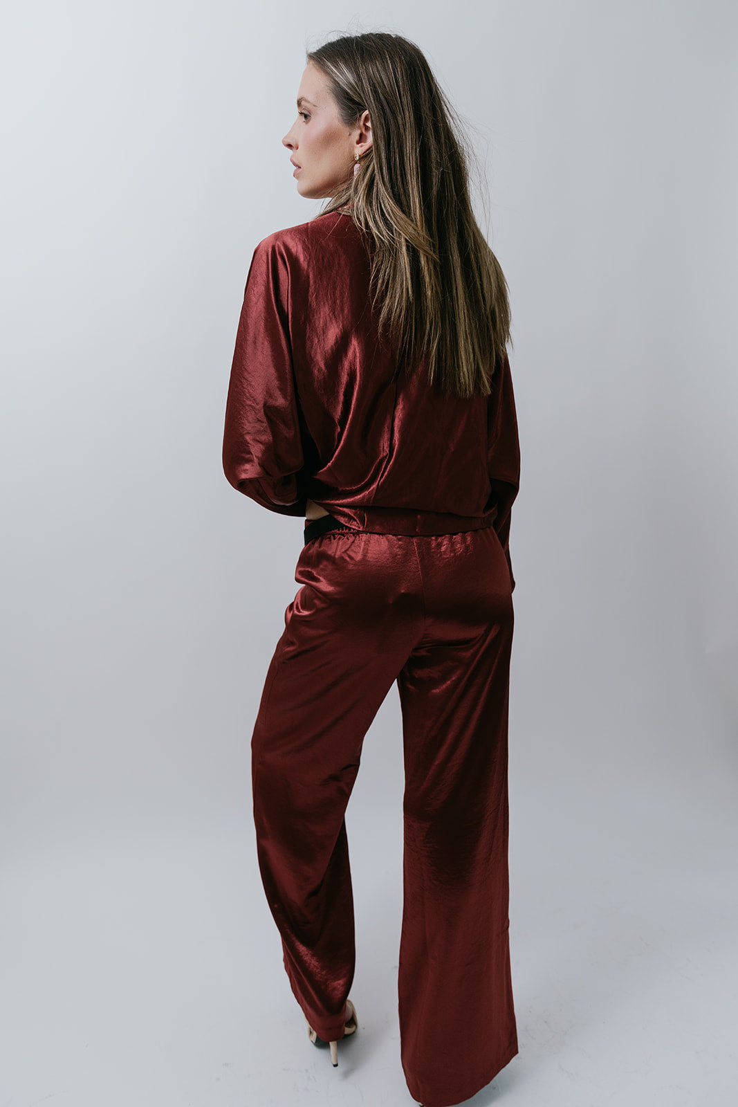 Woman wearing a burgundy satin outfit on a white background, back
