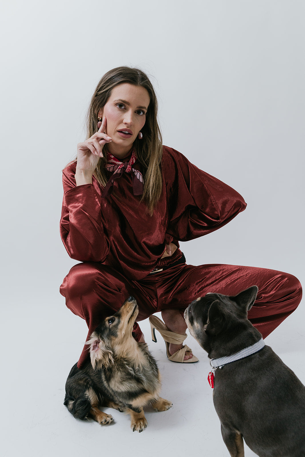 Woman in red silk outfit sitting with two dogs on a white background