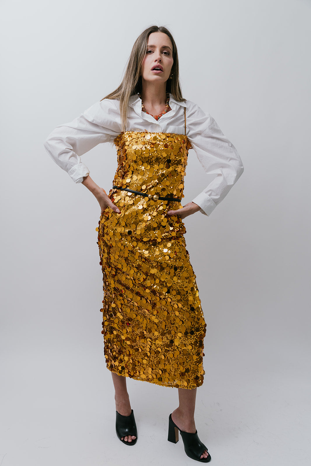 Woman wearing a gold sequin dress over a white shirt on a plain background