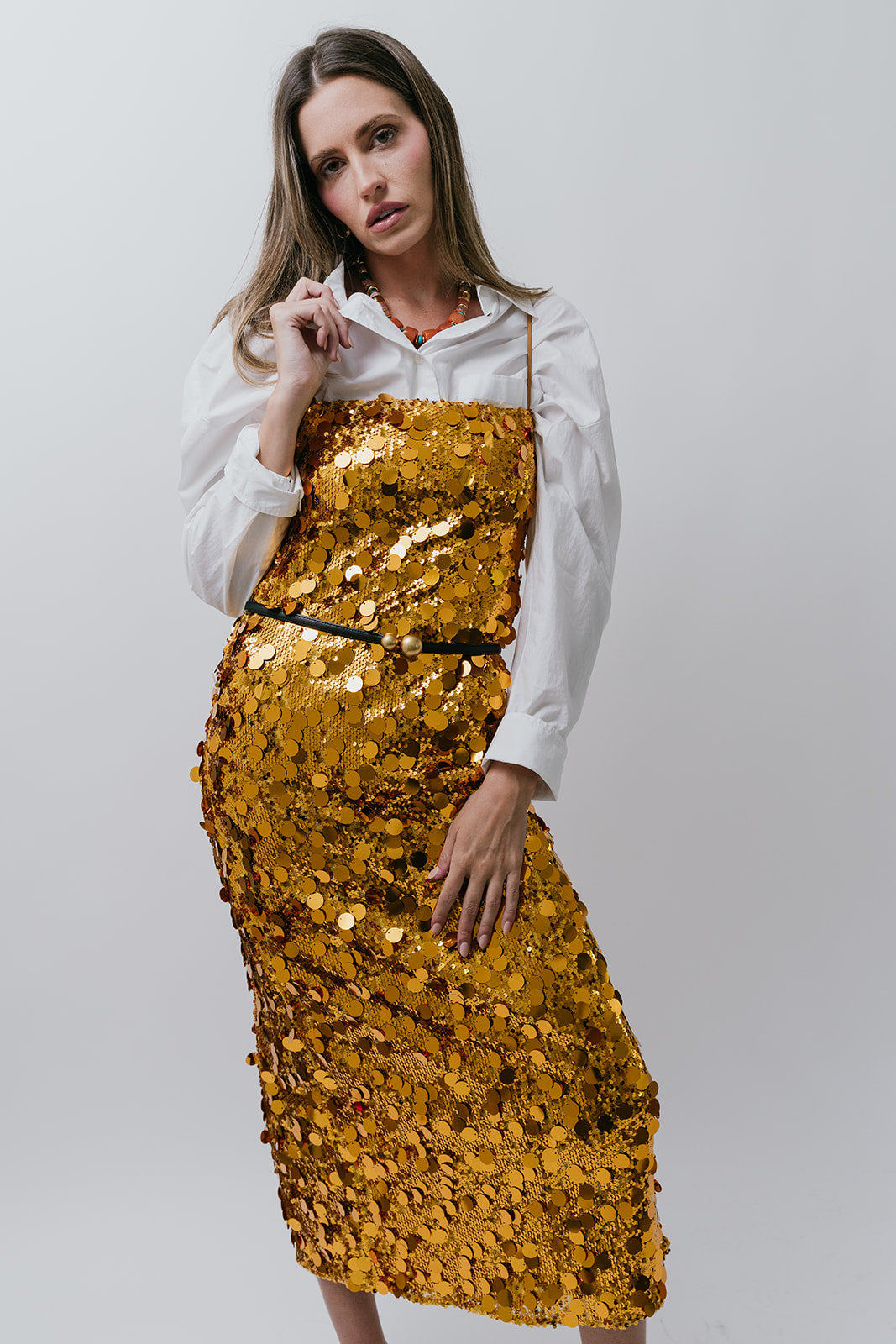 Woman wearing a gold sequin dress over a white shirt on a plain background