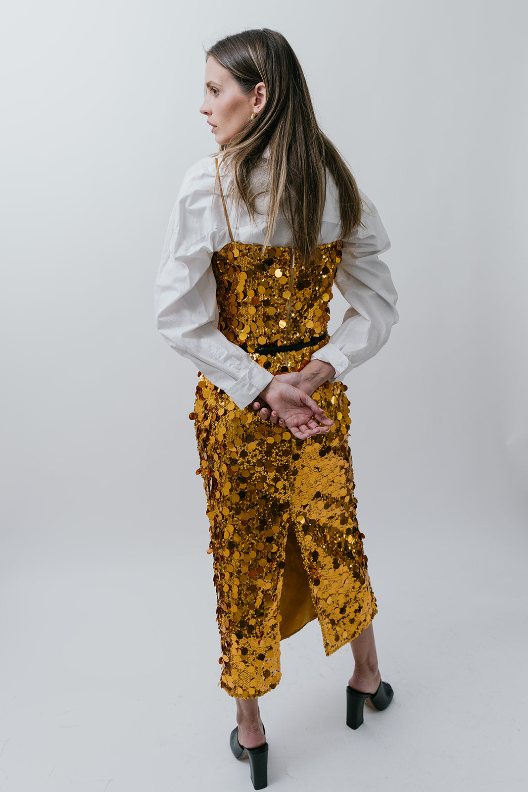Woman wearing a gold sequin outfit on a white background back view