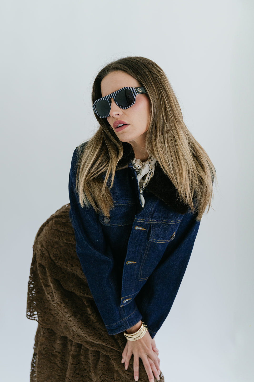 Woman wearing a denim jacket and sunglasses against a white background