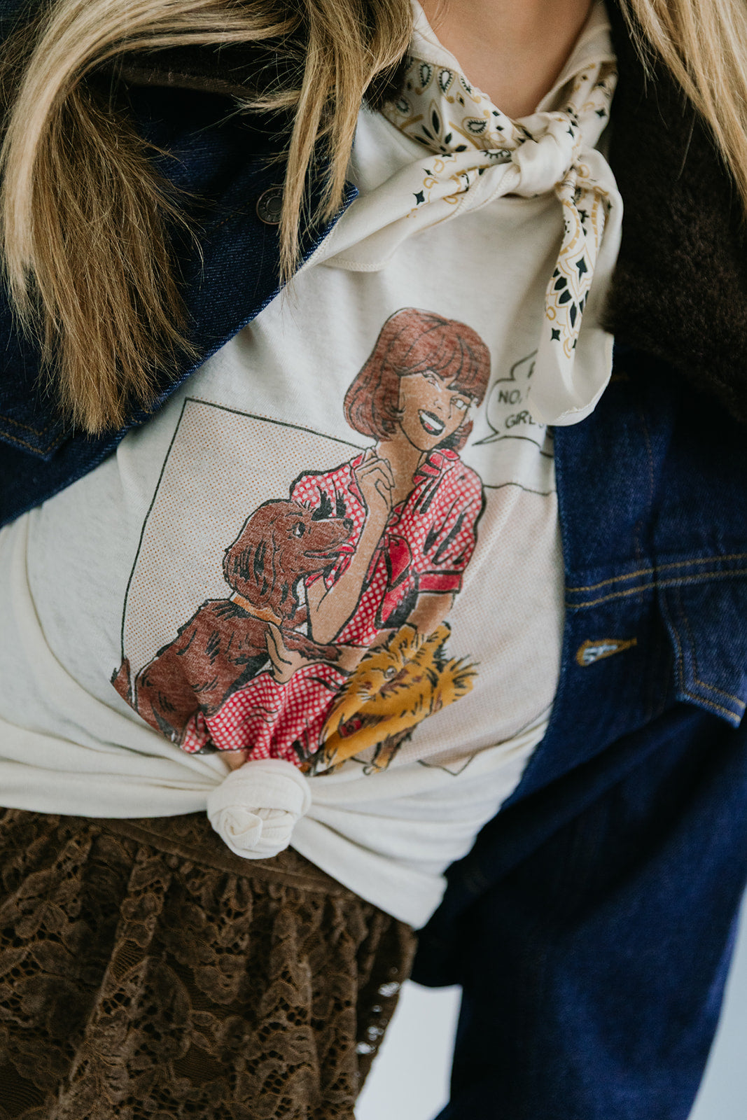 Person wearing a shirt with a graphic design of a woman holding a dog, paired with a patterned scarf and dark jacket.
