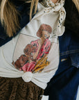 Person wearing a shirt with a graphic design of a woman holding a dog, paired with a patterned scarf and dark jacket.